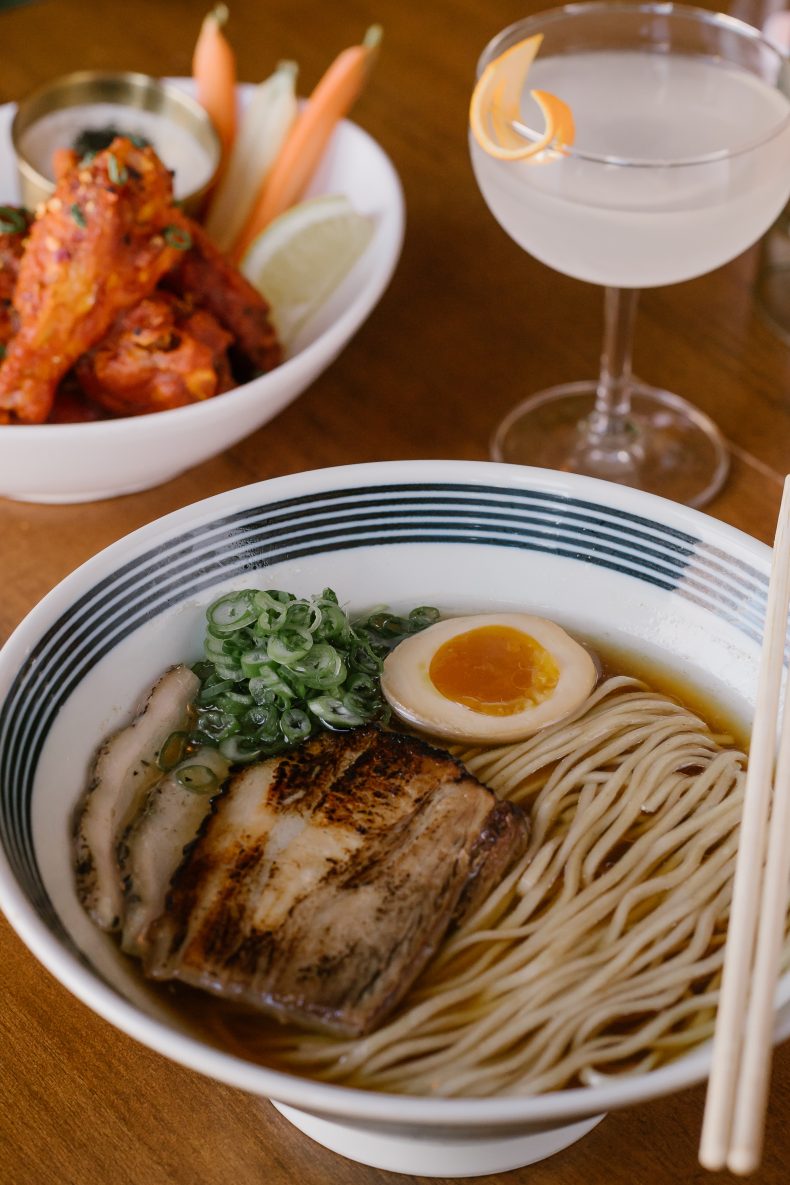 Bowl of ramen with chashu pork and a soft egg, with chicken wings and a martini