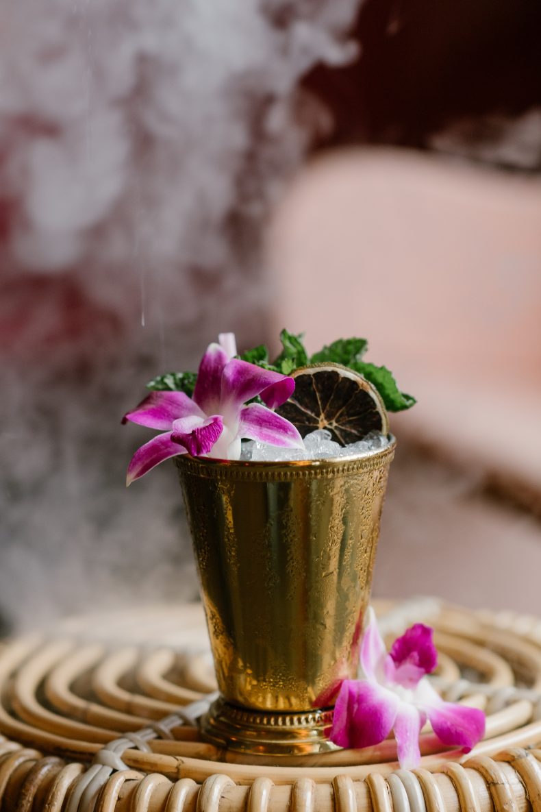 Julep-style cocktail in a gold cup with orchids